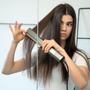 Frau stylt ihr Haar mit dem Aerova Airstrait Luftglätter vor dem Spiegel – glattes Haar dank innovativer Lufttechnologie.